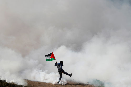 شاب فلسطيني يحمل العلم وسط الغاز