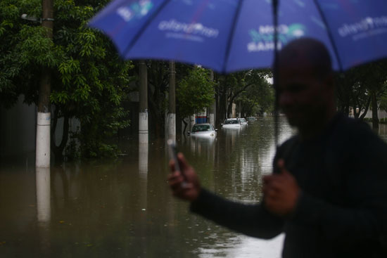رجل يفحص هاتفه في شارع غمرته المياه بعد هطول أمطار غزيرة في حي فيلا ليوبولدينا