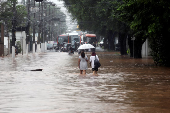 نساء يمشون في شارع غمرته المياه بعد هطول أمطار غزيرة في حي بوتانتا في ساو باولو