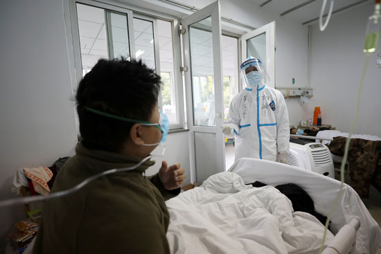 عامل طبي يرتدي بدلة واقية يتفاعل مع مريض داخل جناح معزول في مستشفى جينتيان في ووهان