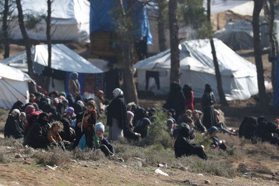 نساء وأطفال مهجرون داخلياً يجلسون خارج الخيام في قرية قاتمة