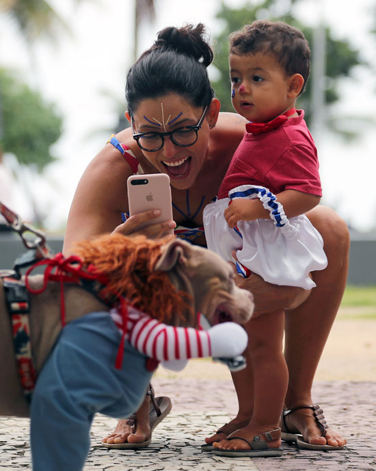 إحد المحتفلات بالكرنفال مع طفلها تلتقط صوراً لكلب أثناء مشاركته في موكب كرنفال الكلاب
