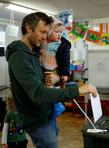 رجل يحمل طفلاً وهو يدلي بصوته في الانتخابات الوطنية الأيرلندية في كورك