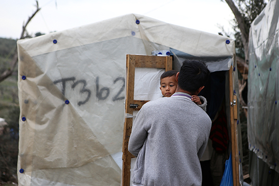 رجل يحمل ابنه خارج مخيم مؤقت للاجئين والمهاجرين بجوار مخيم موريا في جزيرة ليسبوس