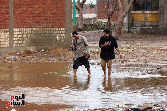 شباب يعبرون مياه الامطار بالشارع