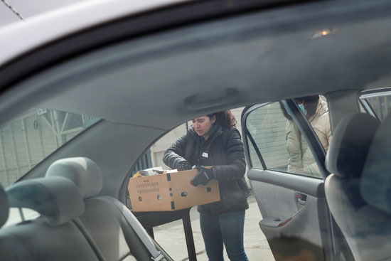 تيل هاردن تحمّل صندوقًا من المواد الغذائية المعبأة مسبقًا على سيارة منتظرة في خط نقل بالسيارة خارج بنك الطعام