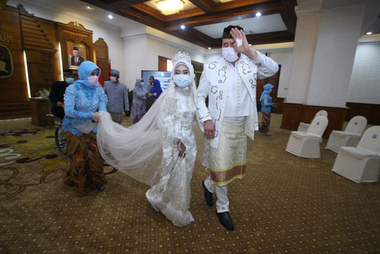 العروس والعريس الإندونيسيان اللذان يرتديان أقنعة واقية للوجه في يوم زفافهما ،