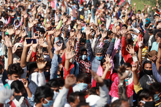 يرفع العمال المهاجرون أيديهم بينما يسألهم رجال الشرطة عن وجهتهم على طول الطريق السريع أثناء عودتهم إلى قراهم