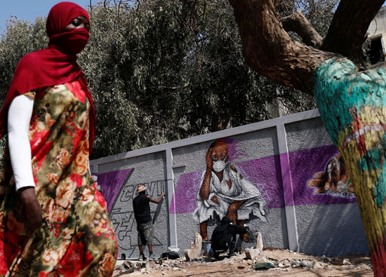 امرأة تمشي أمام فناني جرافيتى وهم يعملون على جدارياتهم لتشجيع الناس على حماية أنفسهم
