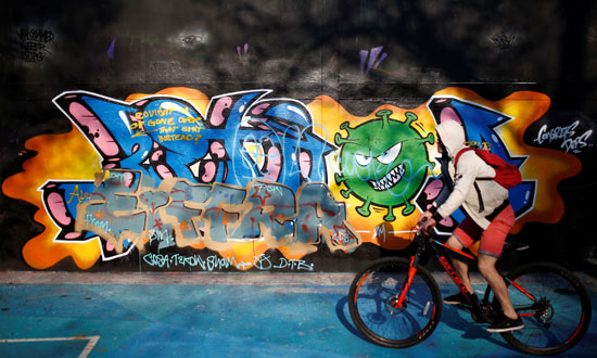 شاب يركب دراجه يمر أمام لوحدة جدارية لكورونا فى لندن