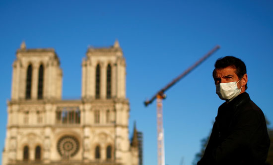 رجل يرتدي قناع وجه يستمع إلى رنين الجرس الكبير بكاتدرائية نوتردام دي باريس