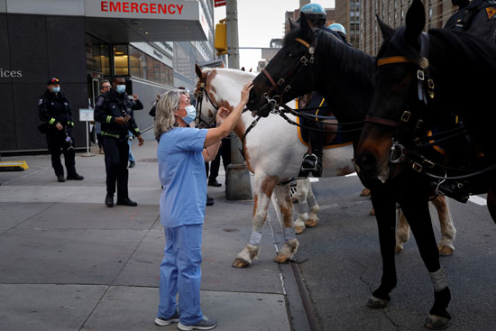 إحدى أفراد الطواقم الطبية تداعب حصان وحدة الخيالة بشرطة نيويورك أثناء تحيتها