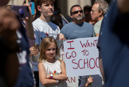 طفلة تقف بجوار لافتة أريد العودة للمدرسة