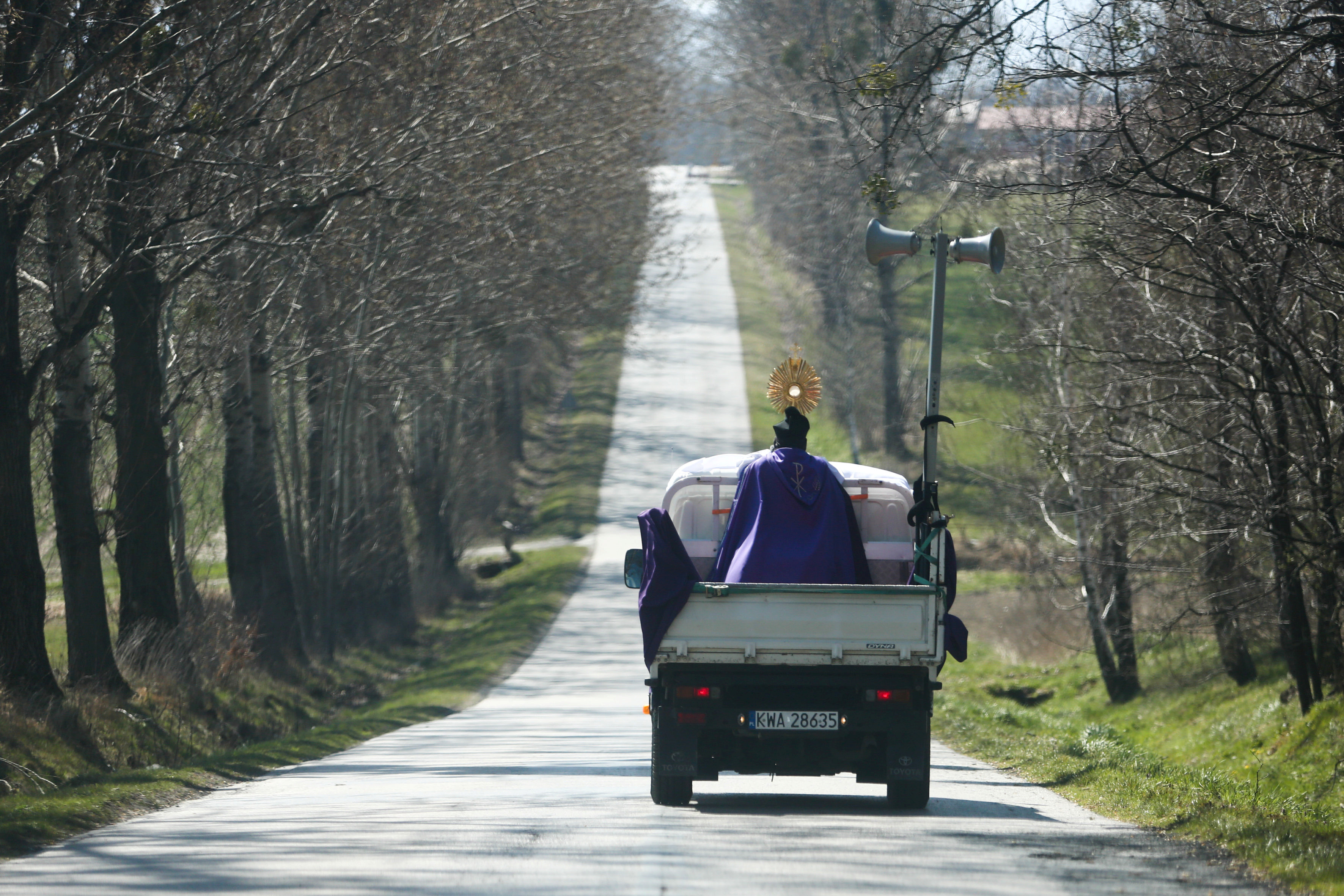 كاهن يرتدي قناعًا وقائيًا يقف على شاحنة صغيرة ويبارك المسيحيين فى القرى خلال أحد الشعانين في نيديك ببولندا