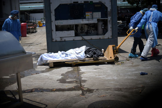 عمال يرتدون معدات واقية يجلبون جثة ميتة عبر حاوية مبردة خارج مستشفى في الإكوادور