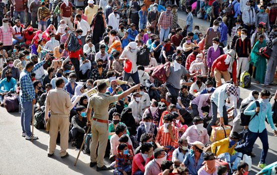 يقوم رجال الشرطة بتوجيه العمال المهاجرين وأسرهم أثناء انتظارهم وصول وسائل النقل إلى محطة السكك الحديدية لركوب القطارات إلى ولايتهم شمال ولاية أوتار براديش