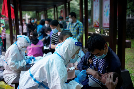 عاملة طبية ترتدي بدلة واقية تجري اختبار الحمض النووي لطفل في مجمع سكني في ووهان