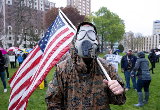 أحد المتظاهرين بالعلم الأمريكي وقناع واقي ضد الغازات