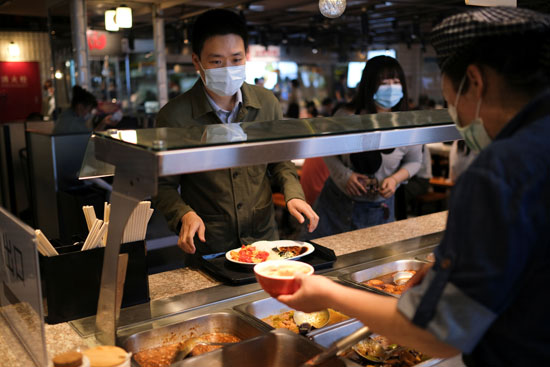 الأشخاص الذين يرتدون أقنعة الوجه يطلبون الطعام في ساحة الطعام في أحد مراكز التسوق خلال وقت الغداء