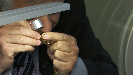 عامل بأحد المحال يفحص القطع الذهبية قبل شرائها من العميل