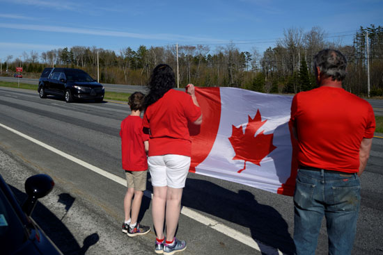 أسرة كندية ترفع علم كندا بانتظار موكب الجنازة