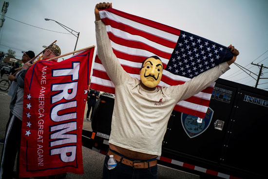 متظاهر يرتدي قناع فانديتا ويحمل العلم الامريكي
