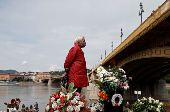 امرأة ترتدي قناع وجه تقف في موقع تذكاري للضحايا في الذكرى السنوية الأولى