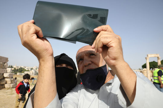 رجل يستخدم أوراق الأشعة لمتابعة كسوف الشمس فى عمان