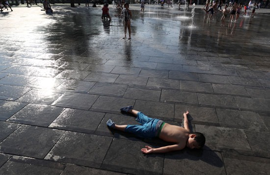 صبي يرقد على الأرض بينما يستريح الأطفال في نافورة في وسط بروكسل