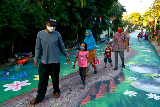 أشخاص يرتدون أقنعة واقية للوجه يمشون أمام جدارية لحديقة وسط تفشى مرض فيروس كورونا