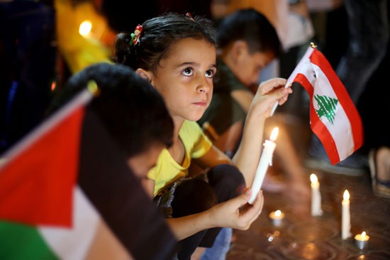 بين علمي لبنان وفلسطين أطفال يحملون الشموع تضامنًا مع ضحايا لبنان
