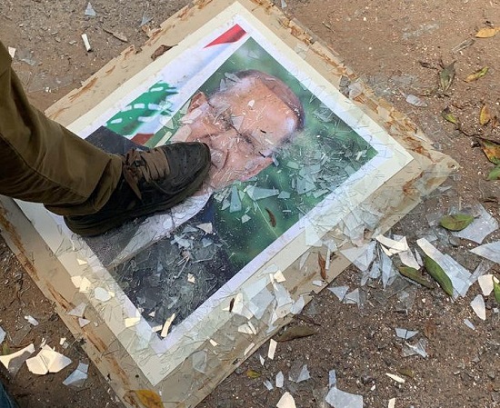 متظاهر يضع قدمه على صورة للرئيس عون