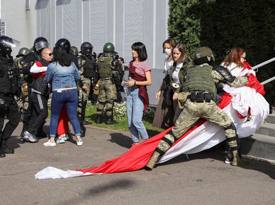 أحد رجال الشرطة يحاول احتجاز متظاهرة تحمل علم بيلاروسيا