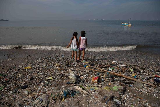 طفلتان ينظران إلى ساحل باسكو المليء بالقمامة في خليج مانيلا