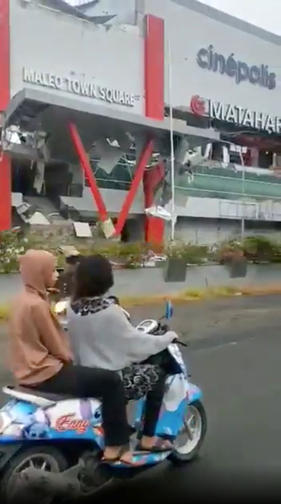 أشخاص يركبون دراجة بخارية بالقرب من مركز تسوق متضرر في أعقاب الزلزال