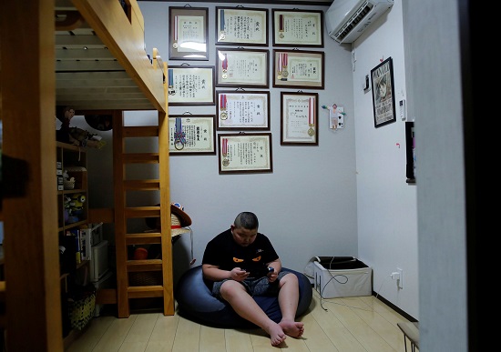 كيوتا يلعب فيديو جيم في غرفته ومن وراءه لوحات الشرف والجوائرز