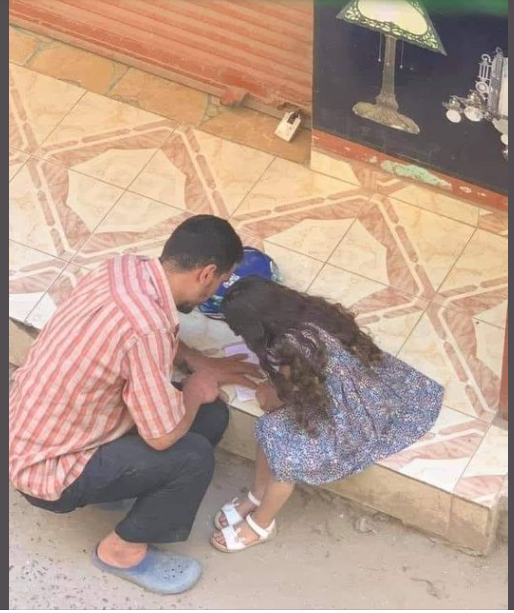 أب يجلس بجوار ابنته فى الشارع لتكملة واجبها المدرسى