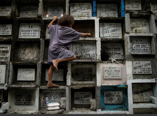 طفل ينظف شمع الشمع الذائب من قبر على طراز شقة في مقبرة مانيلا الجنوبية