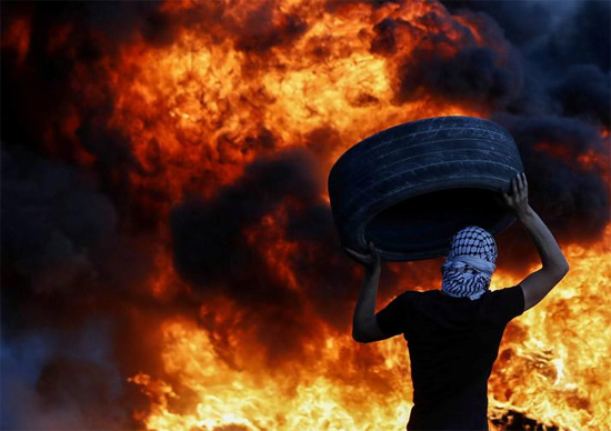 متظاهر فلسطيني يحمل إطارًا وسط الاستعدادات لمظاهرة ليلية ضد المستوطنات الإسرائيلية