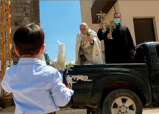 كاهن يقف على شاحنة صغيرة أثناء زيارته للأحياء لمباركة المؤمنين خلال أحد الشعانين