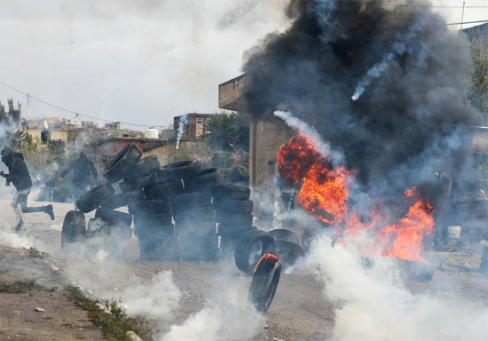 متظاهرون فلسطينيون يركضون بالقرب من الإطارات المحترقة خلال احتجاج على المستوطنات اليهودية