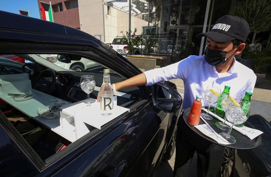 نادل يقدم الطعام للعملاء في سيارتهم خارج مطعم في الكويت
