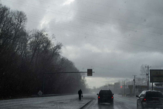 رجل يسير في عاصفة بَرَد بينما تتجه سيارة فريق الاستجابة السريعة لزيارة عميل آخر