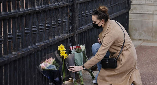 امرأة تضع باقة من الزهور على أبواب قصر باكنجهام