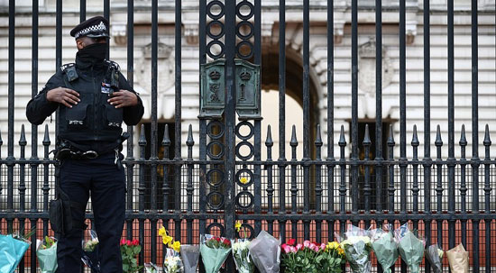ضابط شرطة يقف بجانب باقات من الزهور خارج قصر باكنجهام