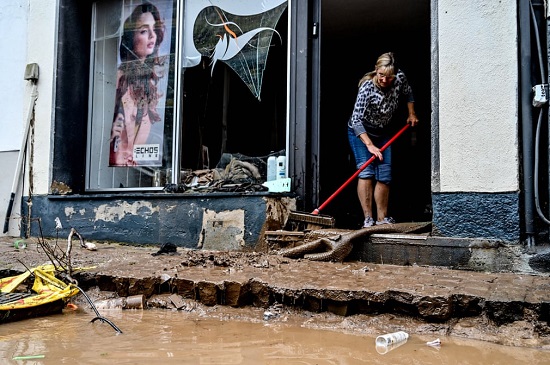 امرأة تمسح مدخل متجر بعد الفيضانات في باد مونستريفيل ألمانيا