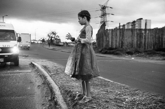فتاة صغيرة تنظر إلى زجاجها البلاستيكي الفارغ وهي تتوسل على الطريق