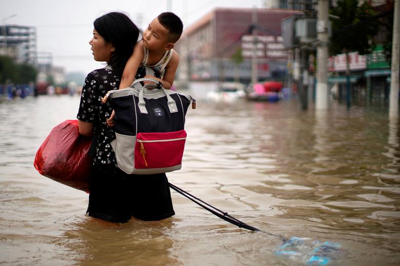 امرأة تحمل طفلاً ومتعلقاتها تخوض في مياه الفيضانات