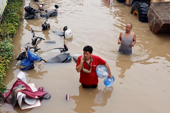 رجل يحمل زجاجات مياه وأطعمة يخوض في مياه الفيضانات
