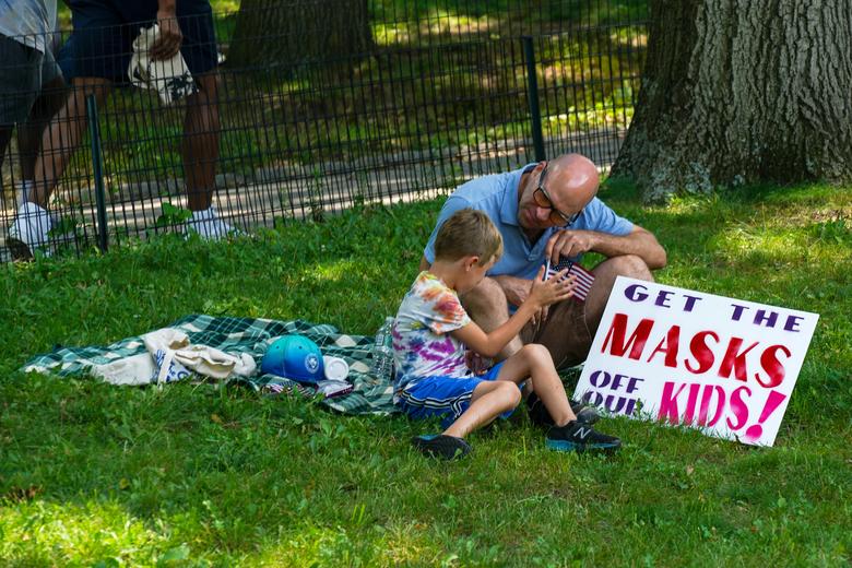 شخص وطفل يجلسان في الظل خلال مظاهرة ضد اللقاح وسط جائحة الفيروس التاجي ، في سنترال بارك ، مدينة نيويورك ،